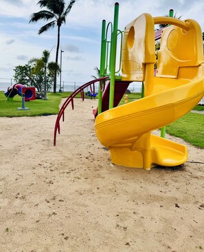 A playground with a yellow slide and green climbing structures.