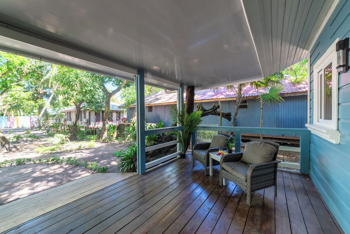 A covered porch with wooden flooring, wicker furniture, and a view of a tropical landscape.