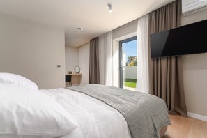Ein modernes Hotelzimmer mit Bett, Schreibtisch, Fernseher und einer Glastür zum Außenbereich.