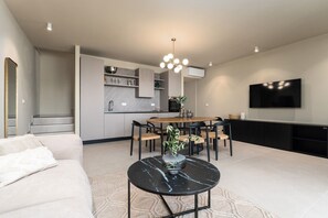Ein modernes Wohnzimmer mit einer Couch, einem Esstisch mit Stühlen, einer Küchenzeile und einem an der Wand befestigten Fernseher.