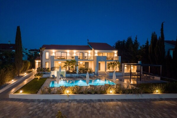 Ein modernes, zweistöckiges Haus mit Swimmingpool, Sitzgelegenheiten im Freien und gut beleuchteter Umgebung.