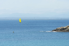 Ein Segelboot auf ruhiger See, im Hintergrund eine felsige Küstenlinie.