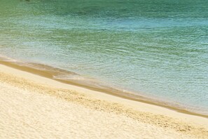 Ein Strand mit klarem Wasser, sandigem Ufer und einer sichtbaren Welle.