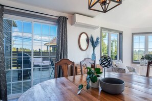 Une pièce spacieuse avec une table à manger en bois, des chaises, une grande fenêtre et une vue sur l’extérieur.
