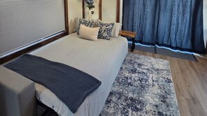 Ein Schlafzimmer mit Bett, Fenster mit Vorhängen, Nachttisch und Holzbalkendecke.