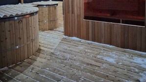 A wooden outdoor sauna area with a glass enclosure and a wooden deck.