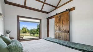 A bedroom with a large window, a bed, a wooden door, and a view of the outdoors.