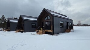 A modern, two-story cabin with a large front porch and a steeply pitched roof, surrounded by snow.