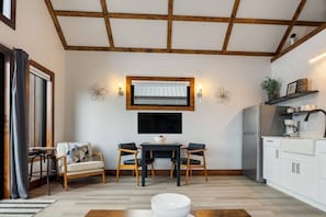 A compact kitchen with a dining area, wooden beams on the ceiling, a flat-screen TV above the table, and a coffee machine on the counter.