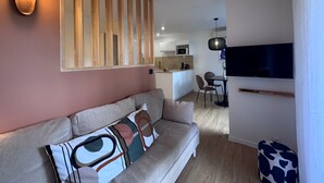 Uma sala de estar moderna com um sofá, uma televisão e uma cozinha ao fundo.