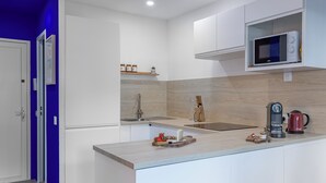Cozinha moderna com armários brancos, micro-ondas, cafeteira e tábua de corte de madeira com alimentos.
