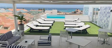 Una terraza en la azotea con sillones de descanso, una piscina y vistas a la playa y al océano.