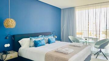 A hotel room with a large bed, a bedside table with a phone, a chair, a small table, and a view of the outdoors.