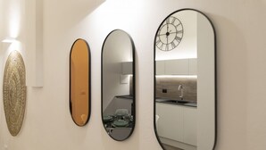Trois miroirs de différentes formes et tailles, fixés au mur, un élément décoratif mural et une horloge avec des chiffres romains.
