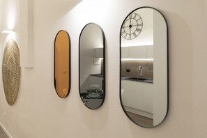 Drei unterschiedlich geformte und große Wandspiegel, eine Dekoration an der Wand und eine Uhr mit römischen Ziffern.