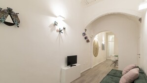 Un salon moderne avec un téléviseur à écran plat, un canapé vert et des œuvres d’art décoratives accrochées au mur.