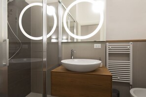 Ein modernes Badezimmer mit Duschkabine aus Glas, einem Holzwaschtisch mit weißem Waschbecken und einem weißen Handtuchhalter.