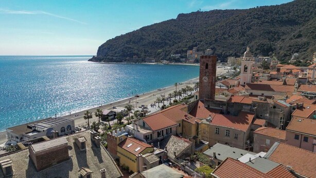 Una località costiera con una torre imponente, edifici a gradoni e una spiaggia.