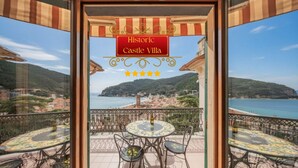 Un balcone con tavolo e sedie, vista mare, e un cartello con la scritta 'Historic Castle Villa'.