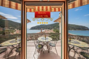 Un balcone con tavolo e sedie, vista mare, e un cartello con la scritta 'Historic Castle Villa'.