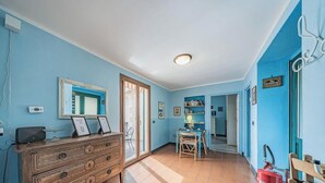 Una stanza con una cassettiera in legno, uno specchio, una libreria e una porta che dà su un'altra stanza.