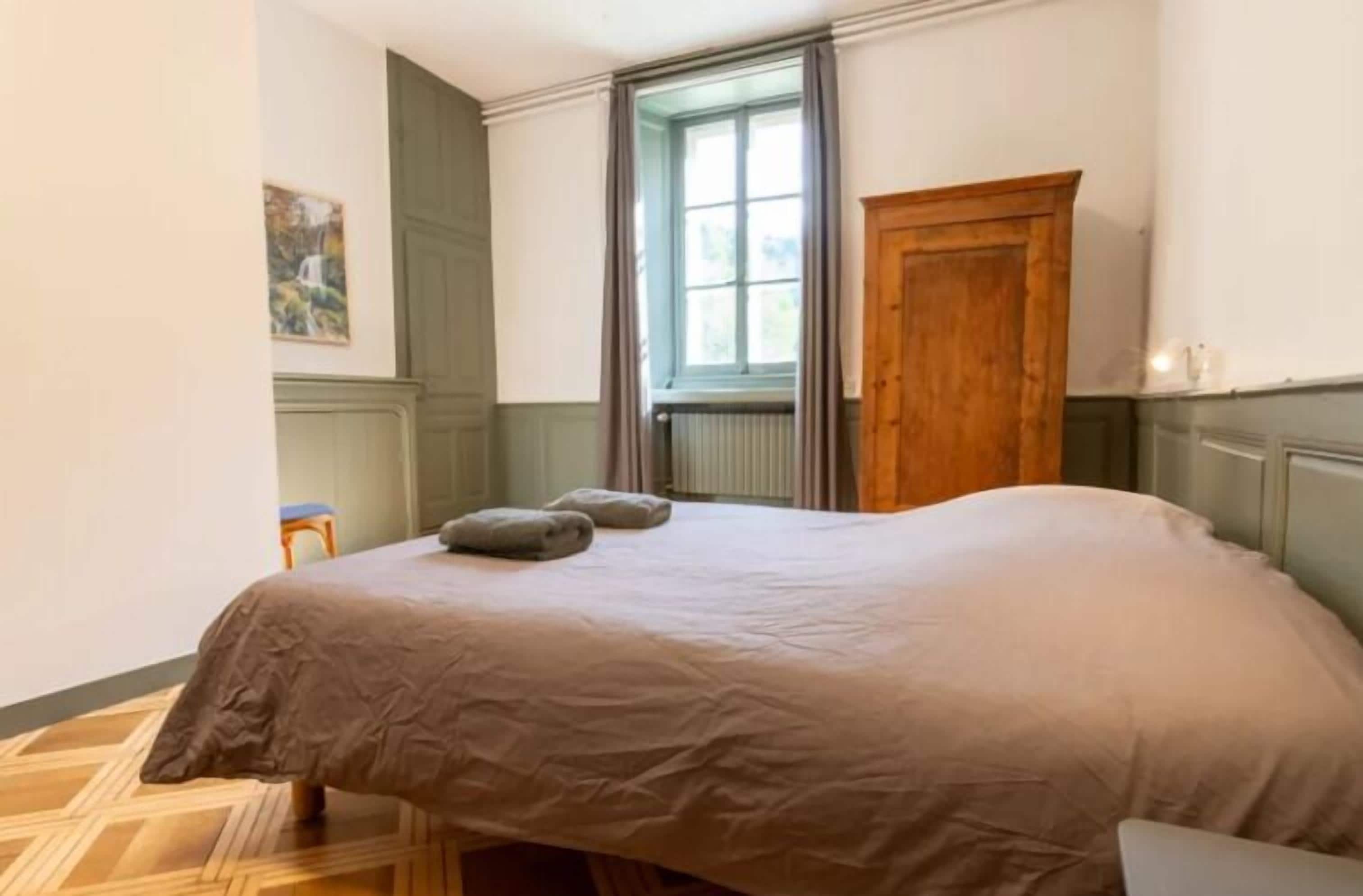 A bedroom with a bed, a wooden wardrobe, a window with curtains, and a radiator.