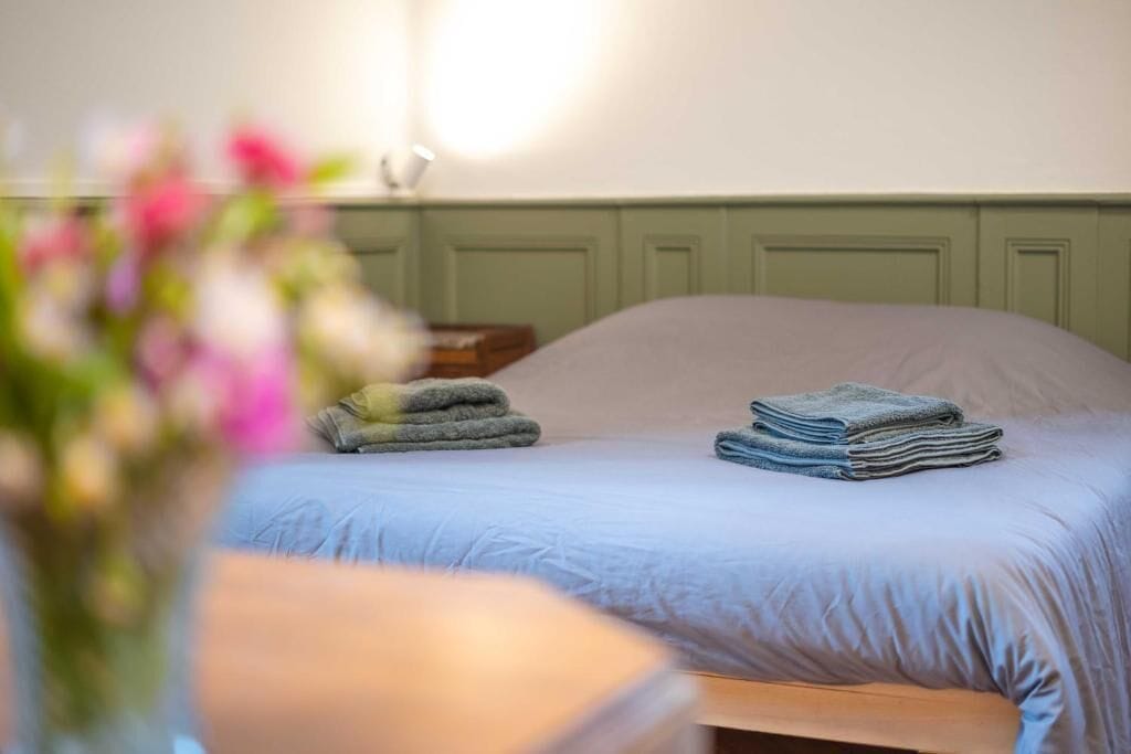 Een bed met een lichtblauwe sprei en twee stapels opgevouwen handdoeken.