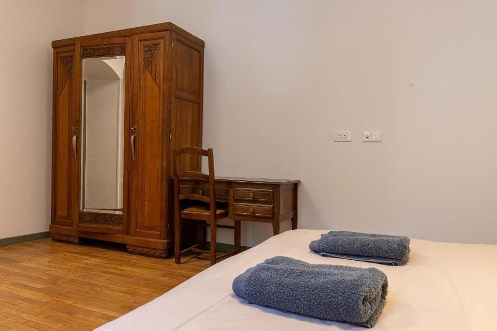 Un dormitorio con un armario de madera, un escritorio de madera, una silla y dos toallas sobre la cama.