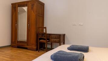 Un dormitorio con un armario de madera, un escritorio de madera, una silla y dos toallas sobre la cama.
