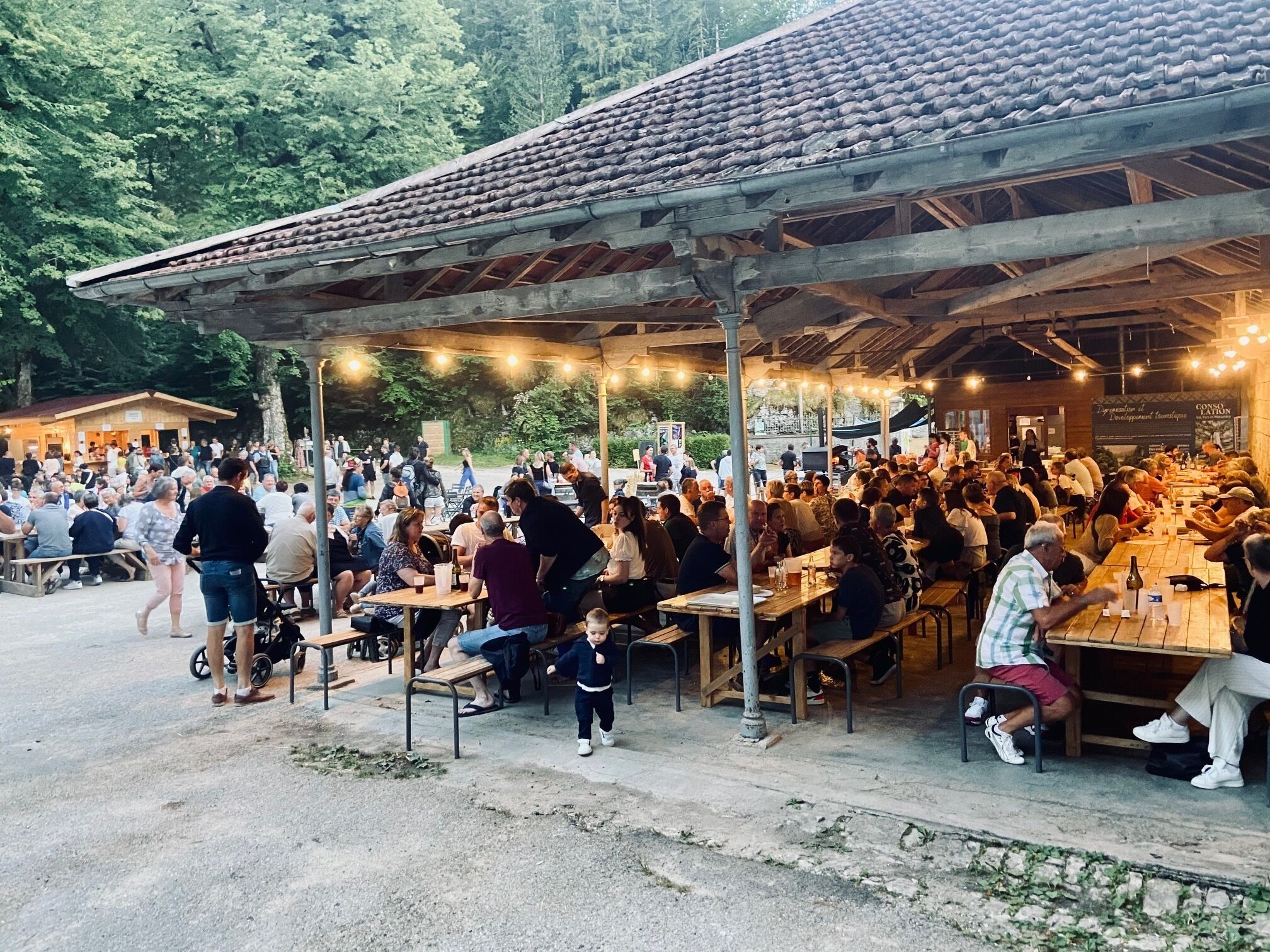 An outdoor dining area with multiple tables and benches, surrounded by a covered structure with a tiled roof.