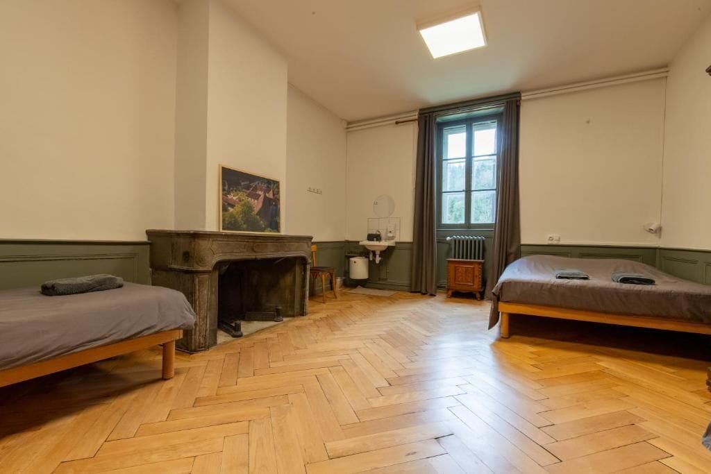 A room with two beds, a fireplace, a window with curtains, and a radiator.
