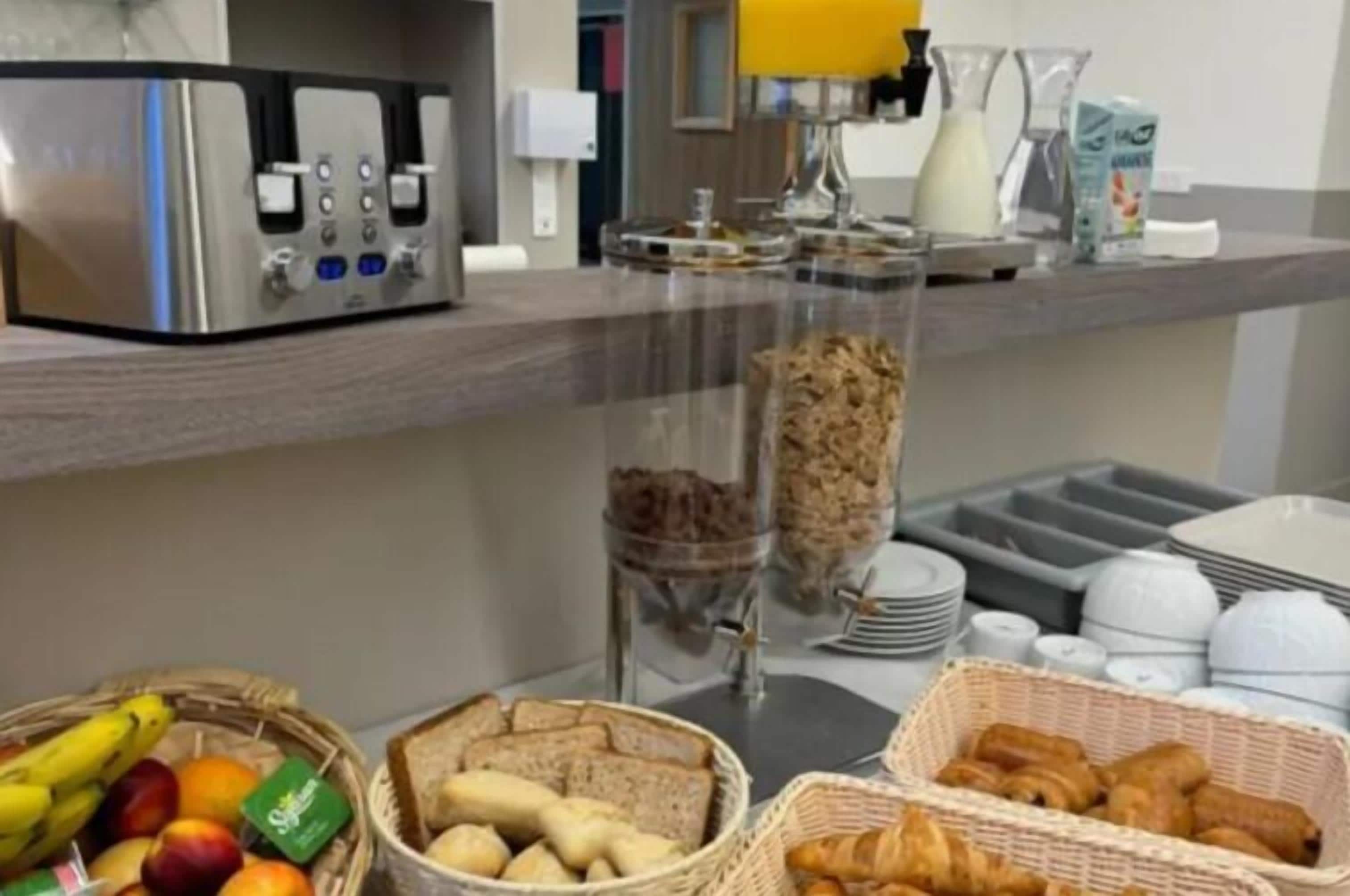 Montaje de un bufé de desayuno con cafetera, cestas de fruta y pan.
