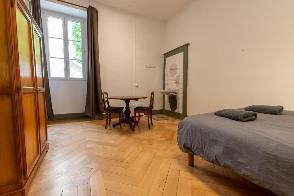 Quarto com cama, mesa, cadeiras, espelho e janela com cortinas.