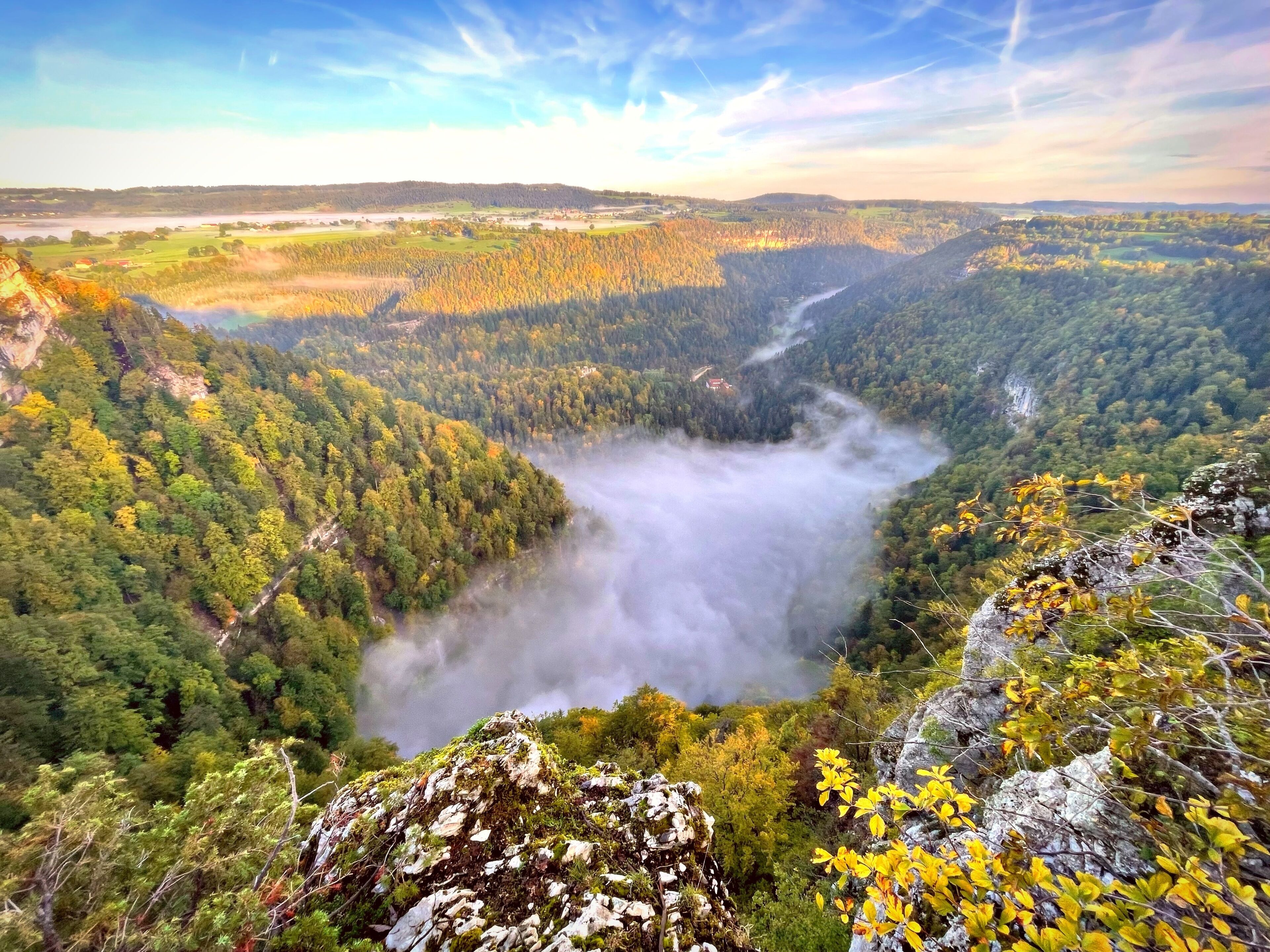 Un paisaje montañoso con un valle, un bosque denso y un río visible.