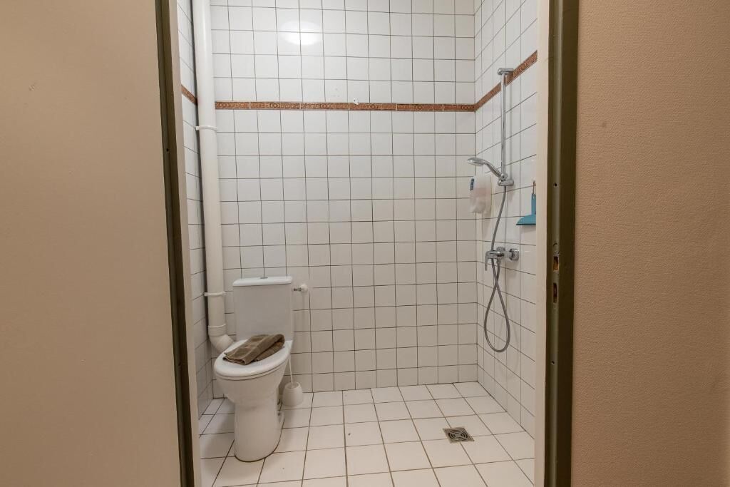 A small, tiled bathroom with a toilet, a shower, and a wall-mounted towel rack.