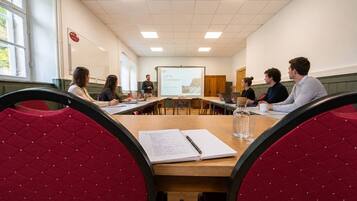 A conference room with a presentation screen, wooden tables, and red upholstered chairs.
