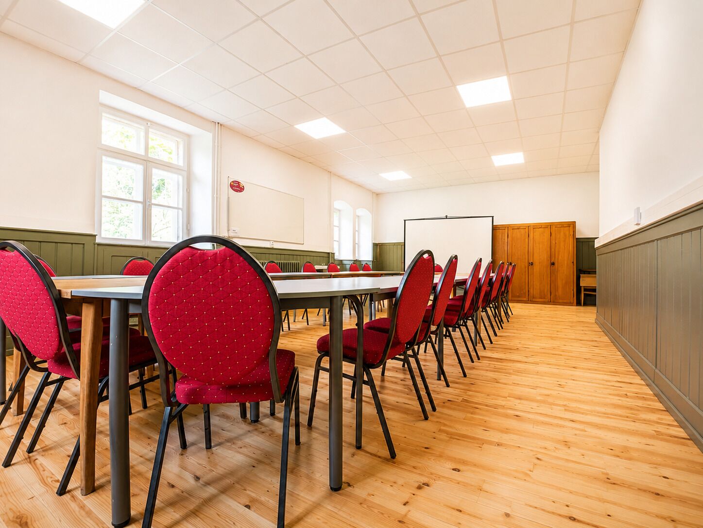 A conference room with a long table, red chairs, a whiteboard, and a projection screen.