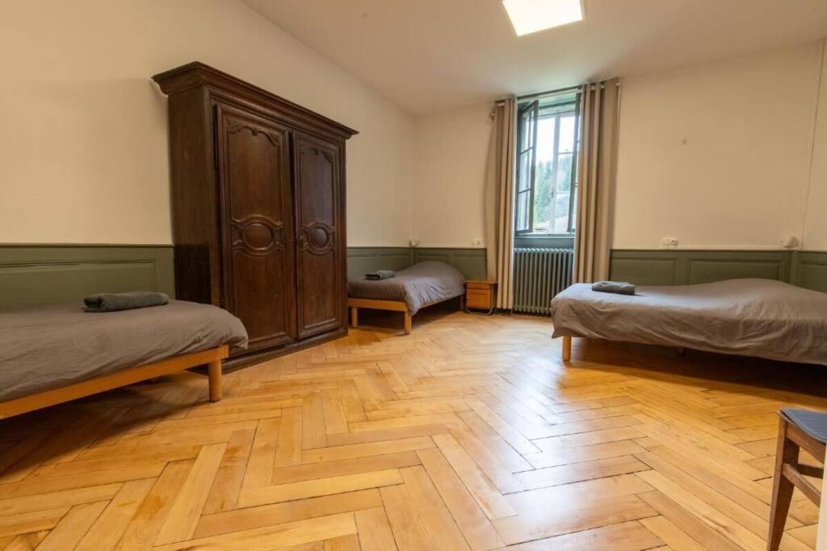 Une pièce avec trois lits en bois, une grande armoire et une fenêtre avec des rideaux.