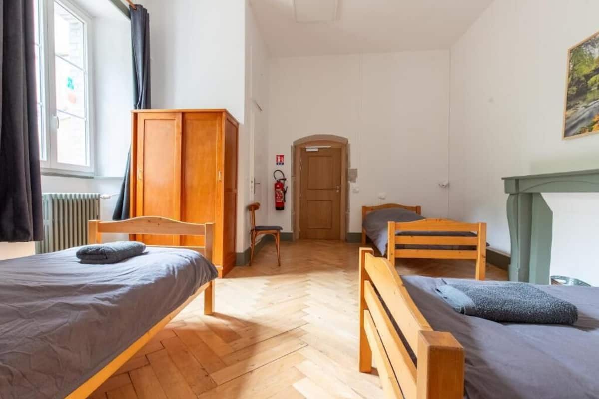 Une pièce comprenant deux lits en bois, une armoire, un radiateur, un extincteur et une porte donnant sur une autre pièce.