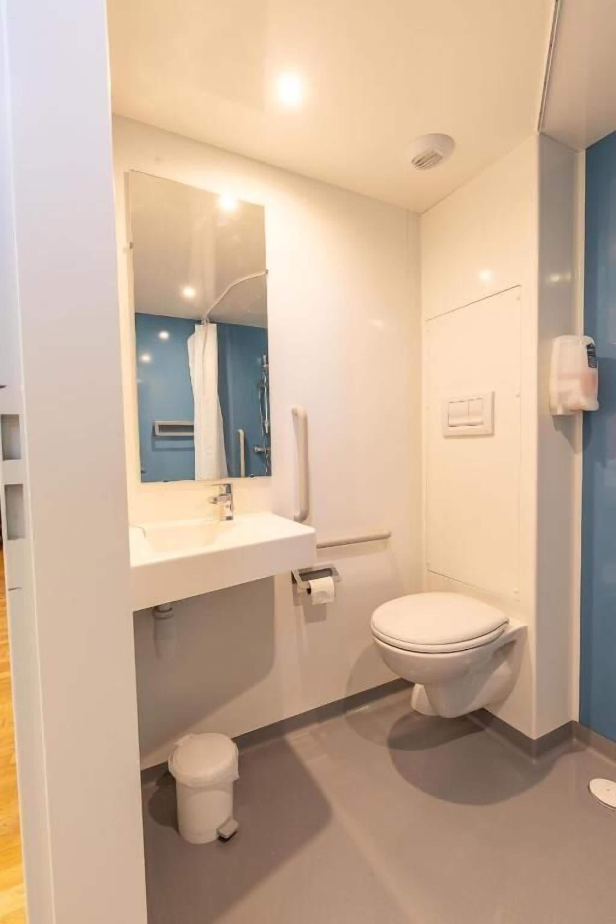 Un baño moderno con inodoro, lavabo, espejo y ducha.