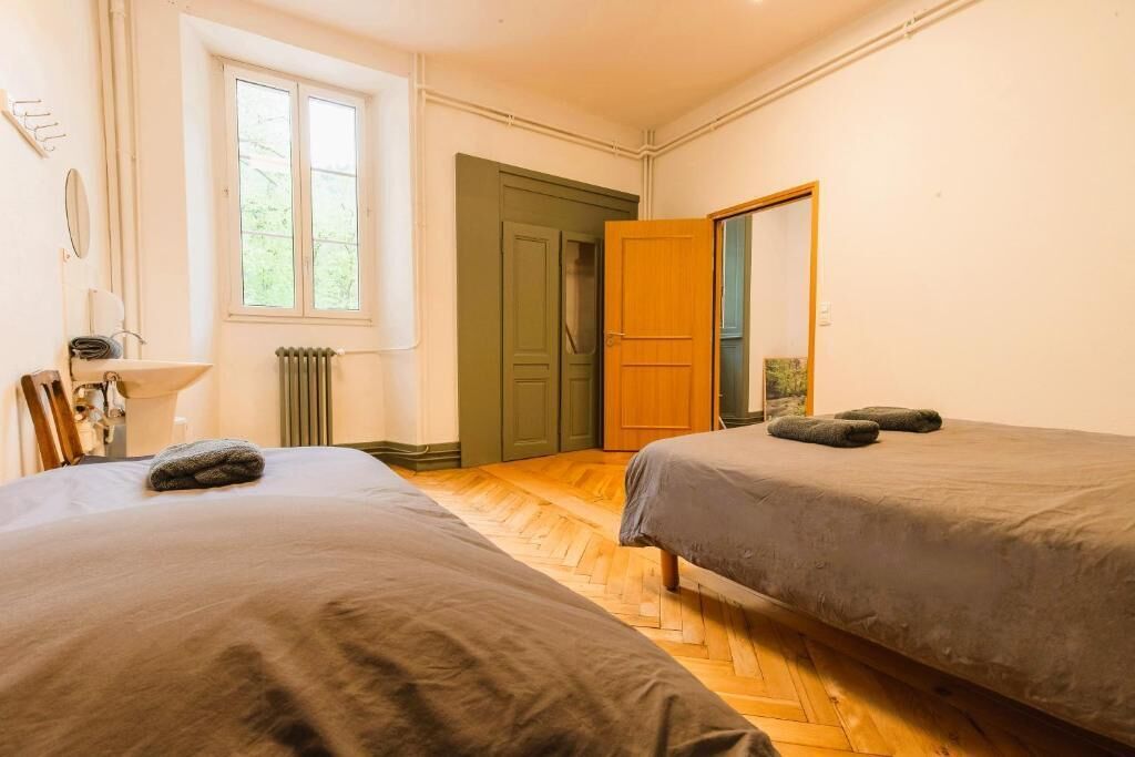 Ein Zimmer mit zwei Betten, einem Heizkörper, einem Fenster und einer Tür.