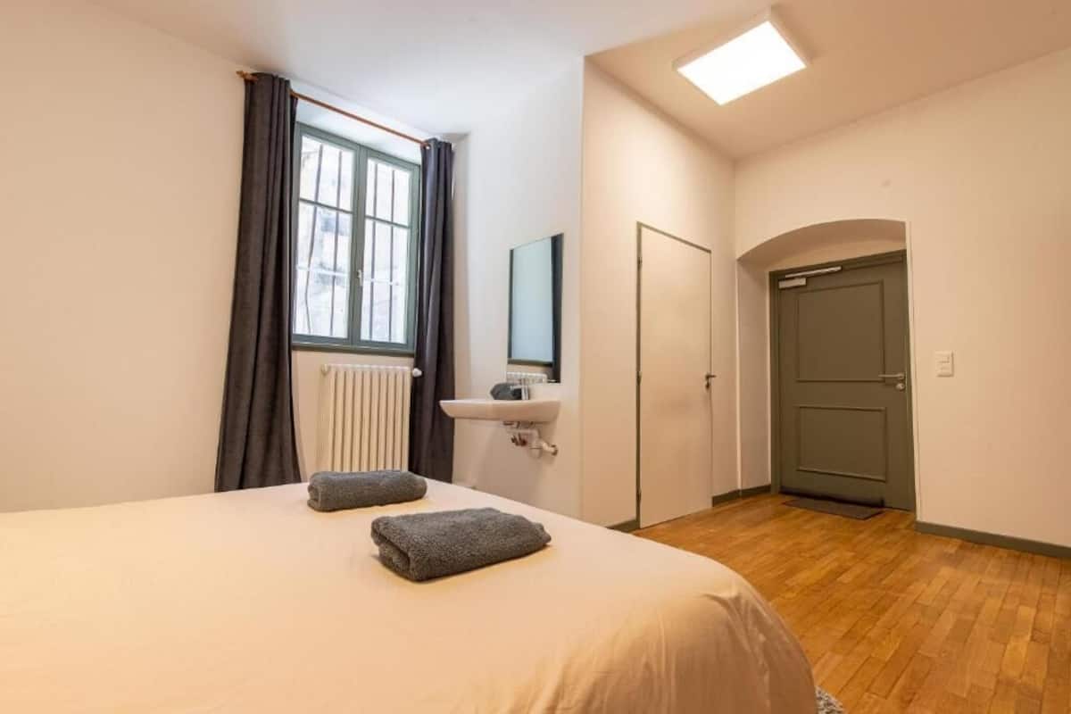 Une chambre à coucher avec un lit, une fenêtre avec des rideaux, un radiateur, un lavabo et une porte.