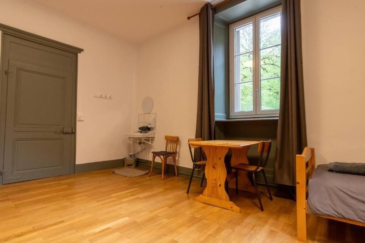 Une pièce avec un plancher en bois, un bureau avec une chaise, un lit et une fenêtre avec des rideaux.