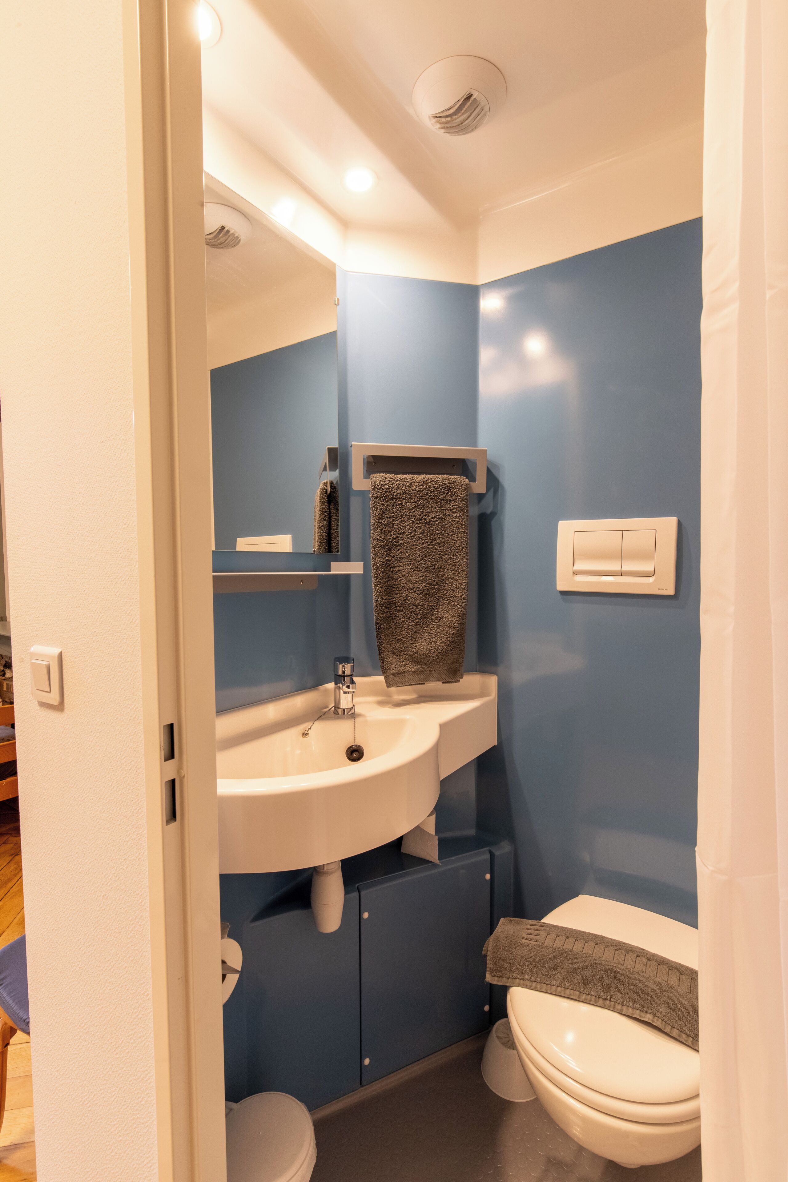 Un baño con lavamanos blanco, paredes azules, un perchero y un inodoro.