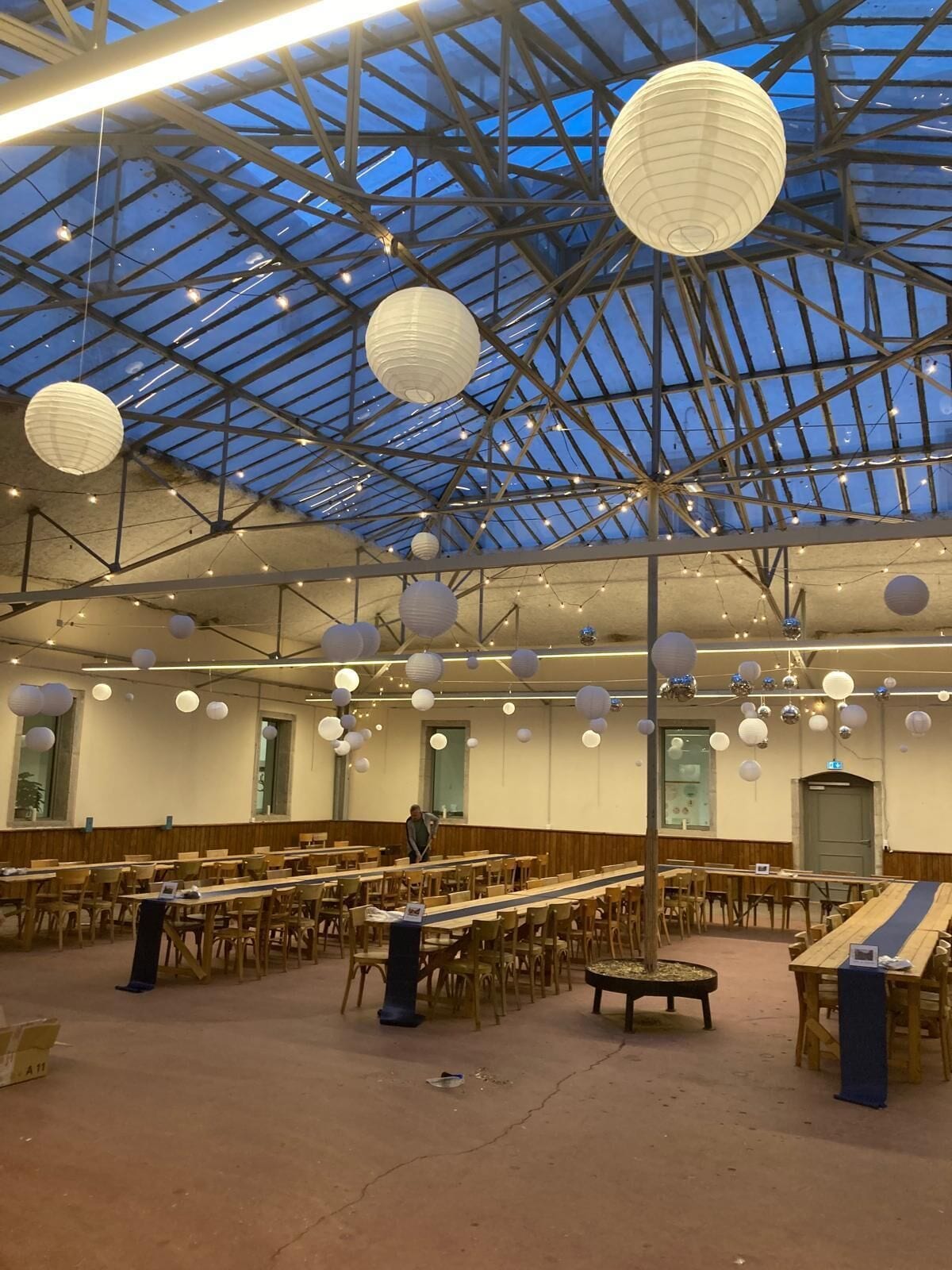 A spacious hall with a high ceiling, wooden tables and chairs, and hanging paper lanterns.