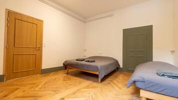 A room with a herringbone wooden floor, two beds with grey bedding, a wooden door, and a green door.