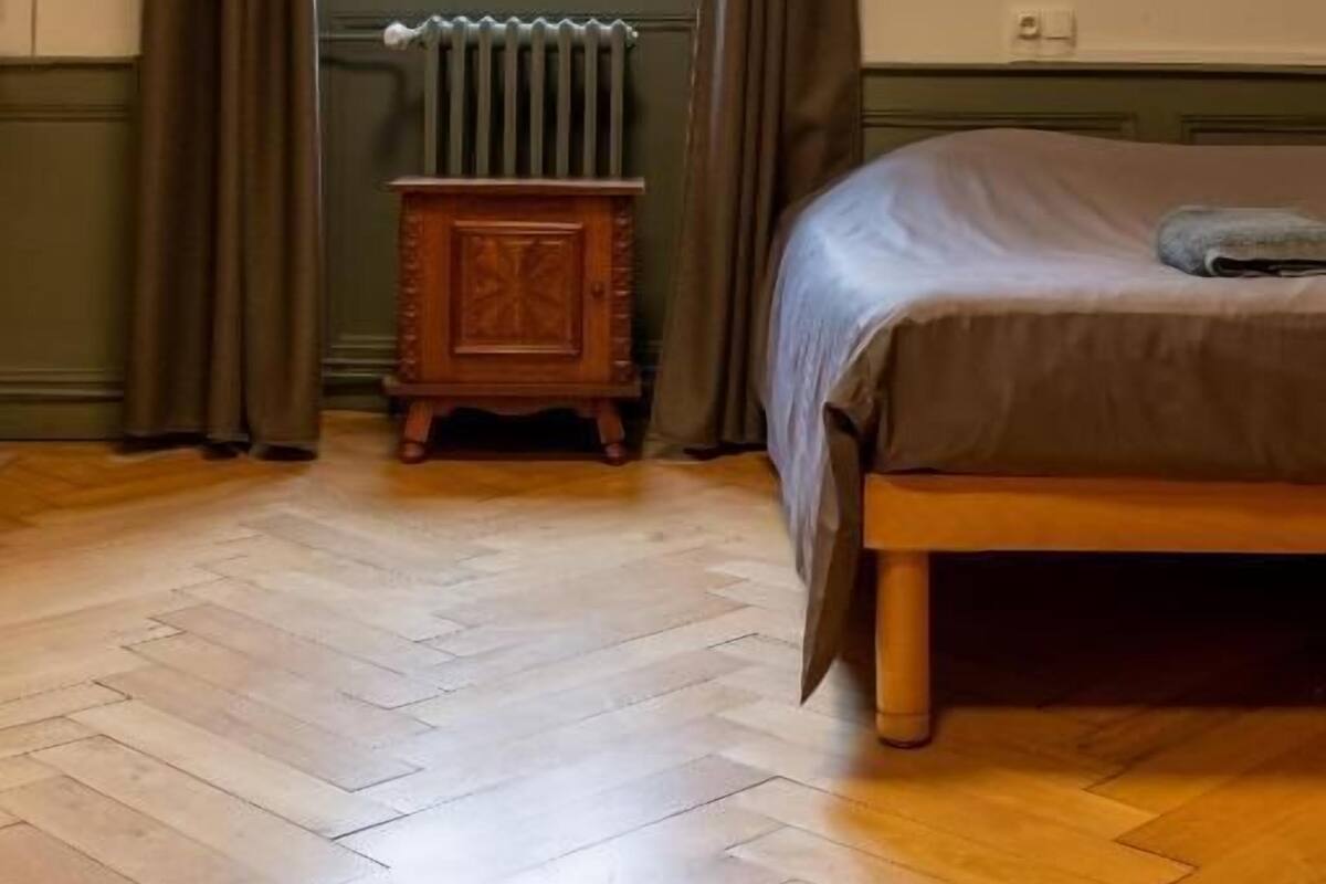Une pièce comprenant un lit, un radiateur, une fenêtre avec des rideaux et une armoire en bois.