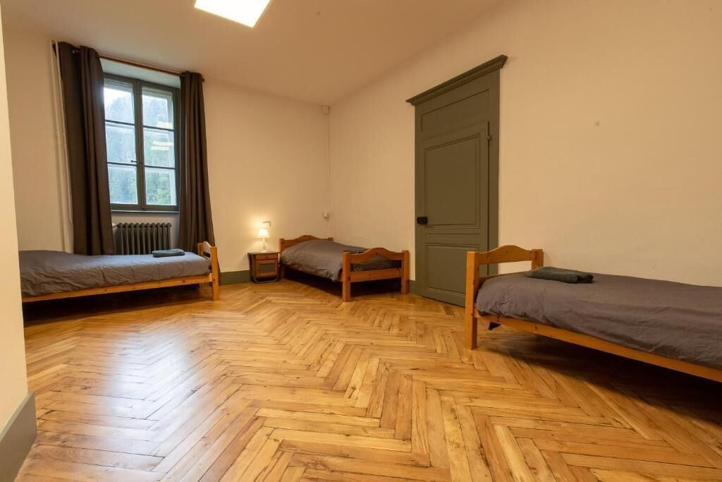 Una habitación con tres camas de madera, un radiador, una puerta y una ventana con cortinas.