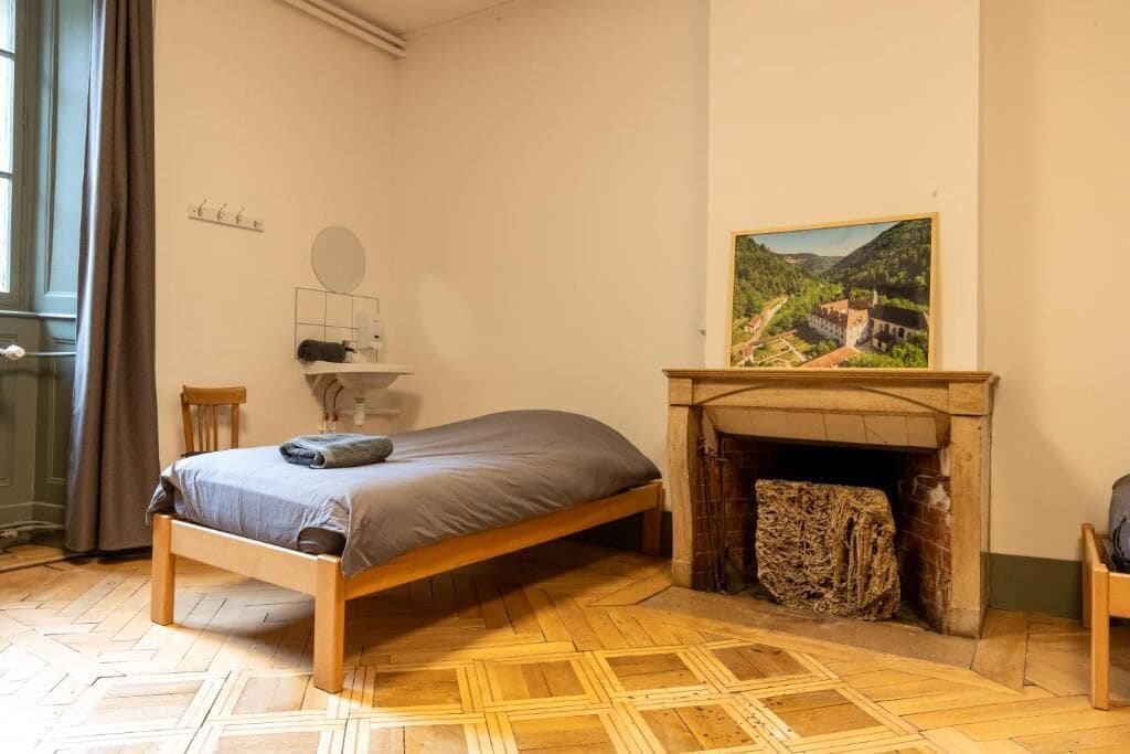 Una habitación con cama, chimenea, un cuadro y una ventana con cortinas.