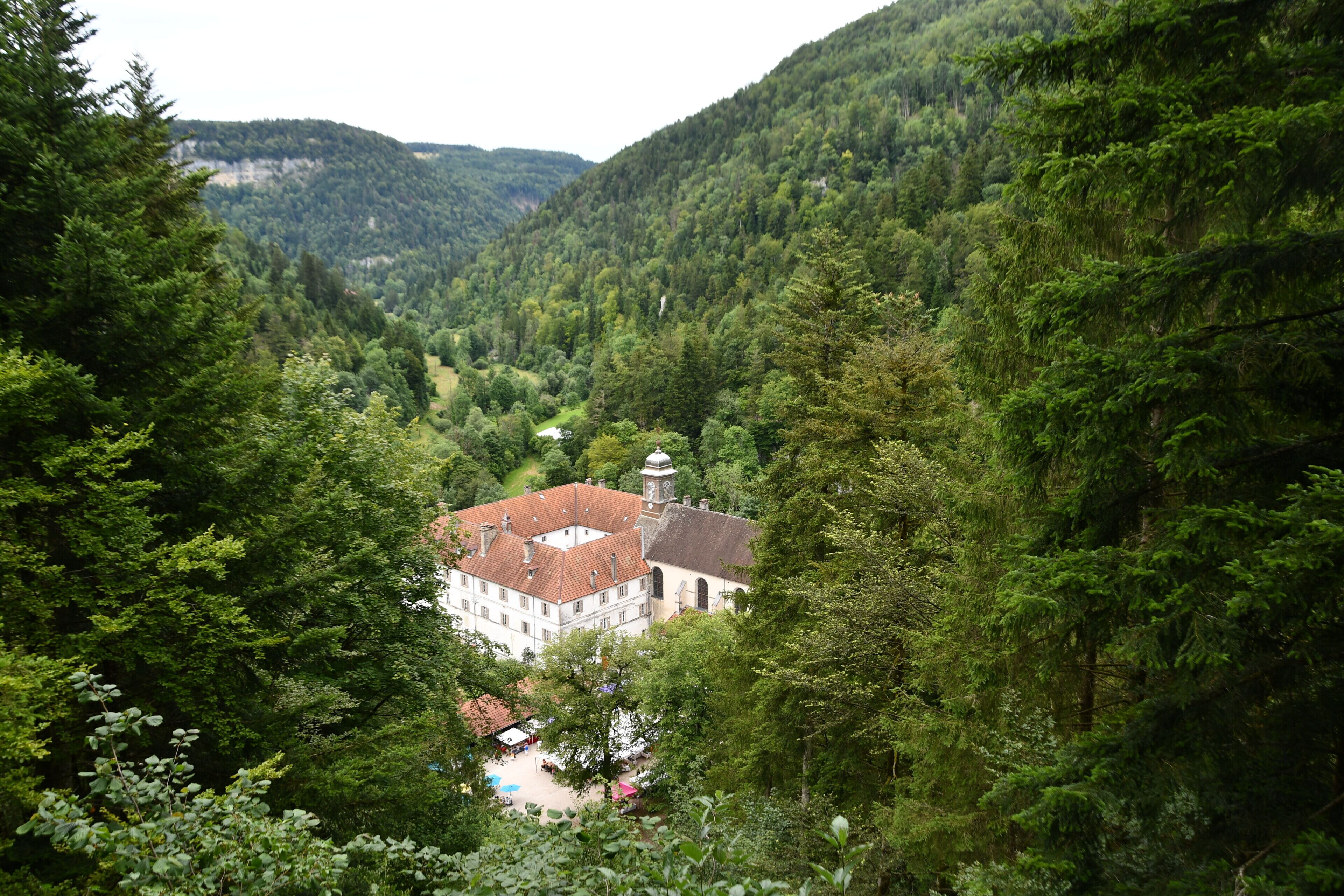 A building with a red-tiled roof nestled among dense green forested hills.